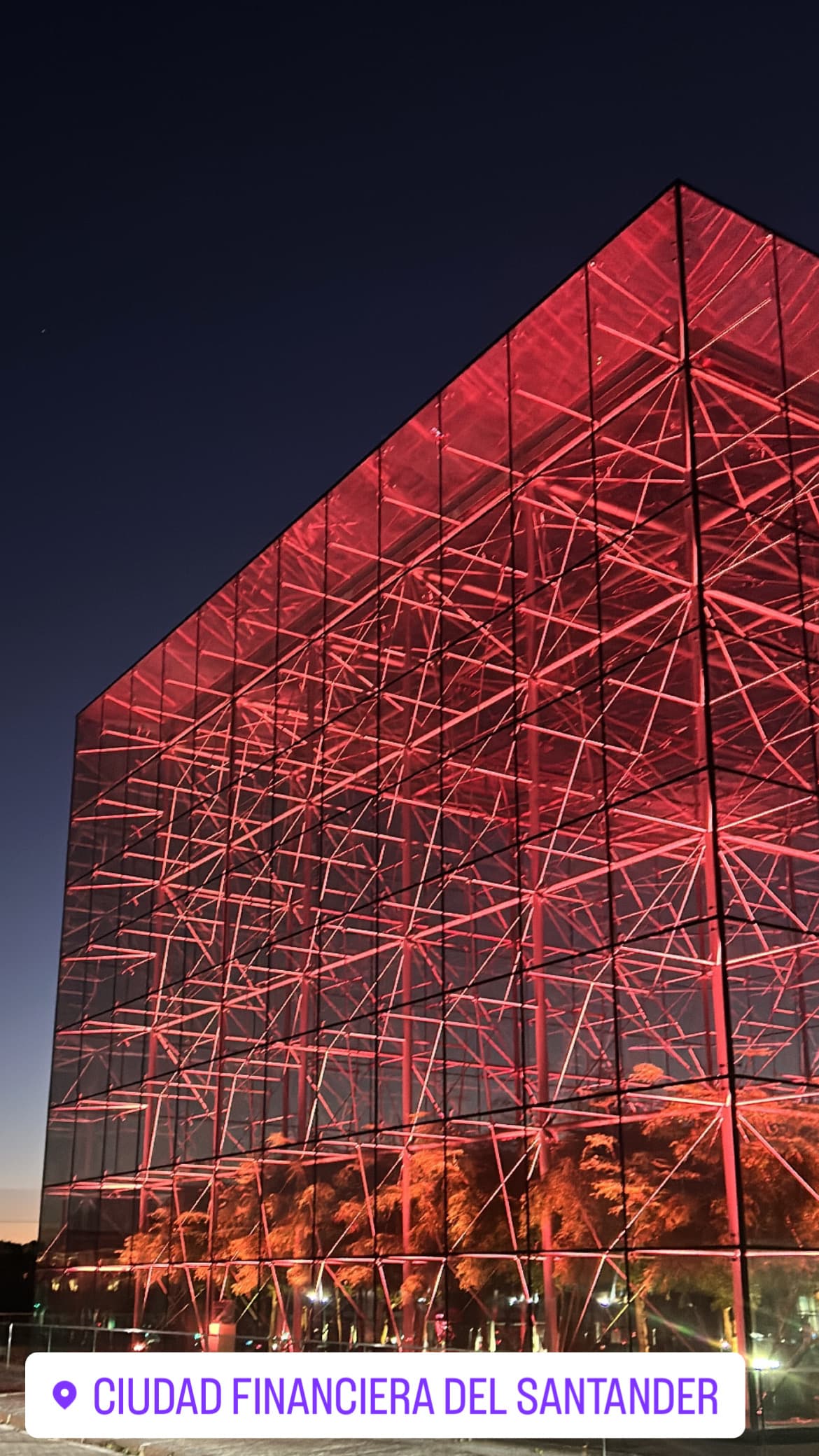 Edificio de cristal con una intrincada estructura interna iluminada de rojo intenso durante la noche.