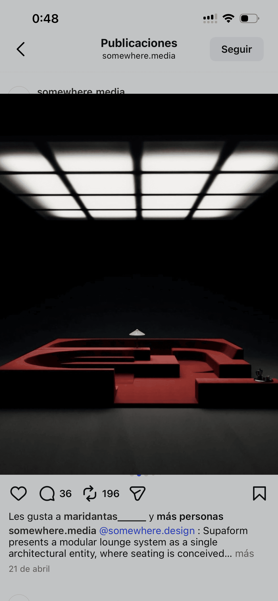 Sofá modular rojo en un espacio oscuro bajo una gran luz de techo cuadriculada.